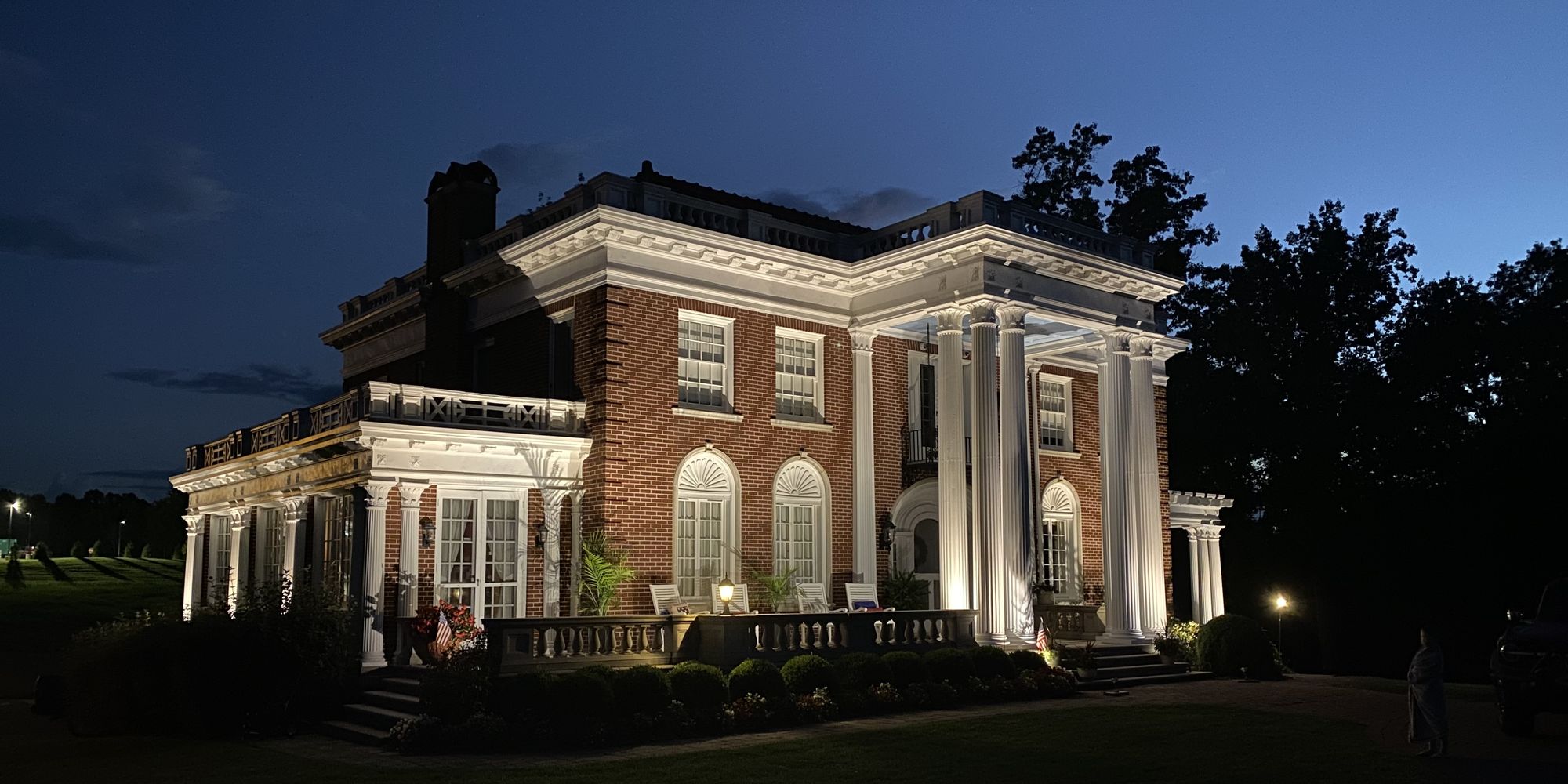A brick Colonial Revival residence at dusk, with architectural uplighting and clipped foundation plantings