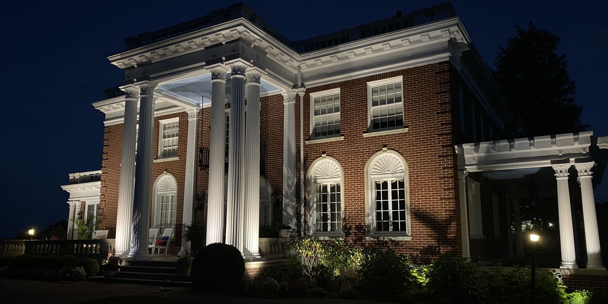 Architectural and landscape lighting picking out the columns and beds of a brick residence at night
