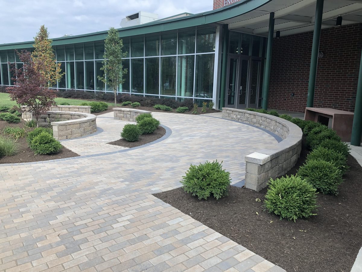 A newly built paver plaza with curved seat walls and fresh plantings at an institutional building