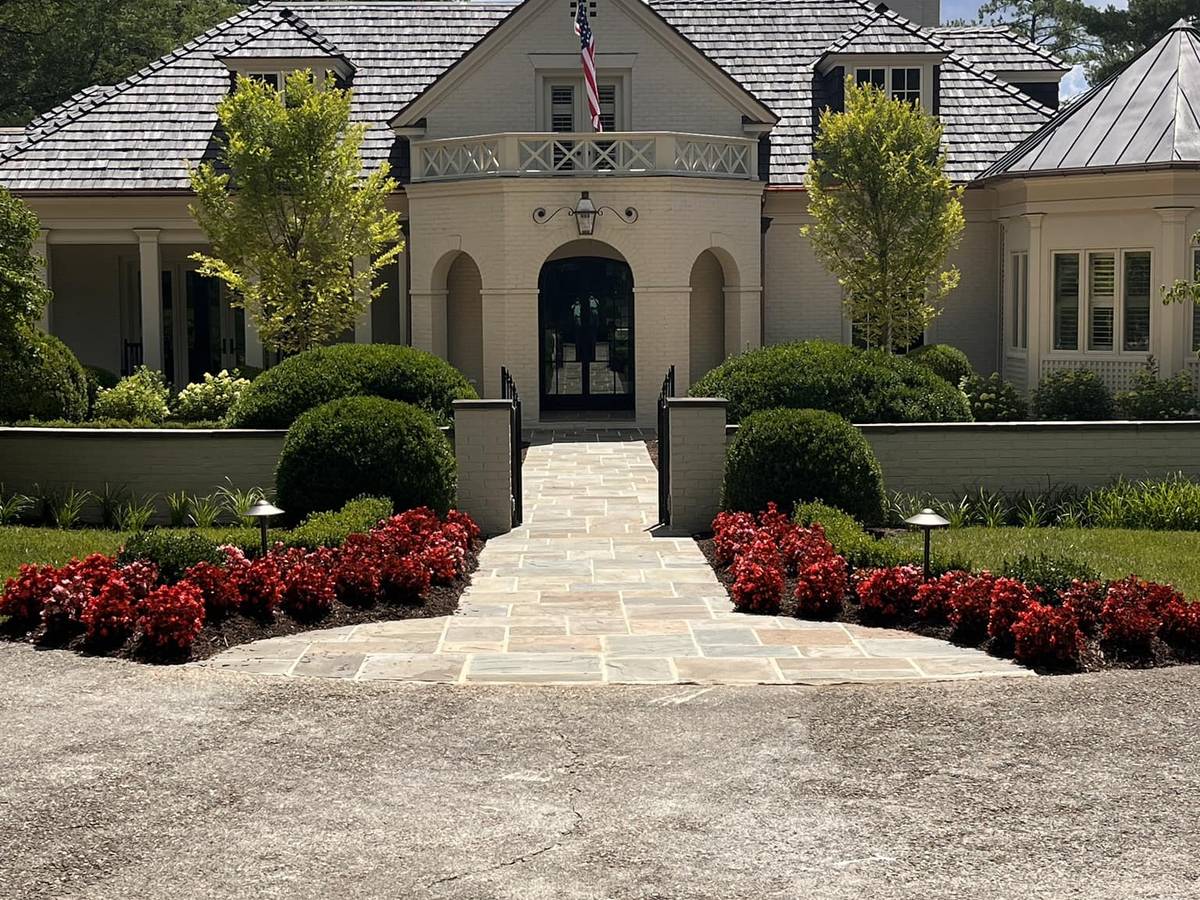 Edged beds, clipped hedging and red azaleas either side of a flagstone entrance walk