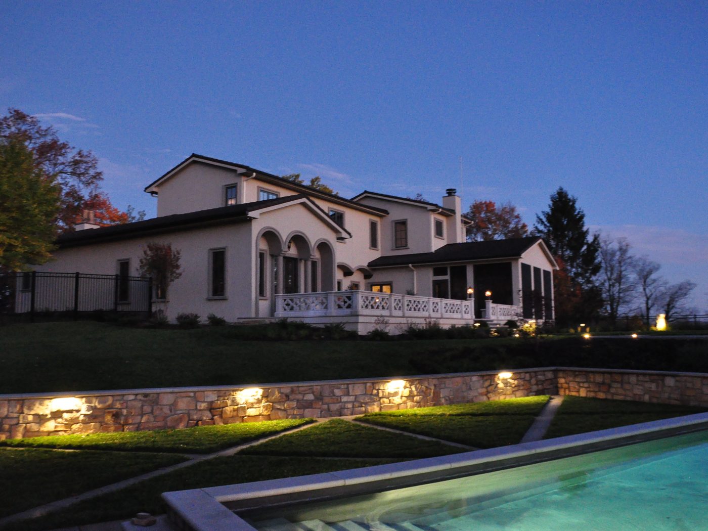 Terraced lawn panels and a lit stone retaining wall beside a pool